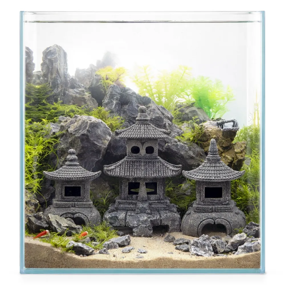 Drei detailreiche japanische Steinlaternen (Pagoden) als Aquarium-Deko vor Felsen und lebenden Wasserpflanzen in einem Glasbecken auf sandigem Bodengrund